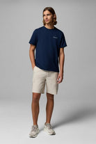 Man wearing a navy t-shirt and beige shorts on a gray background