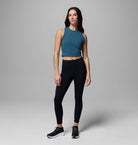 Woman wearing a teal crop top and black leggings on a gray background