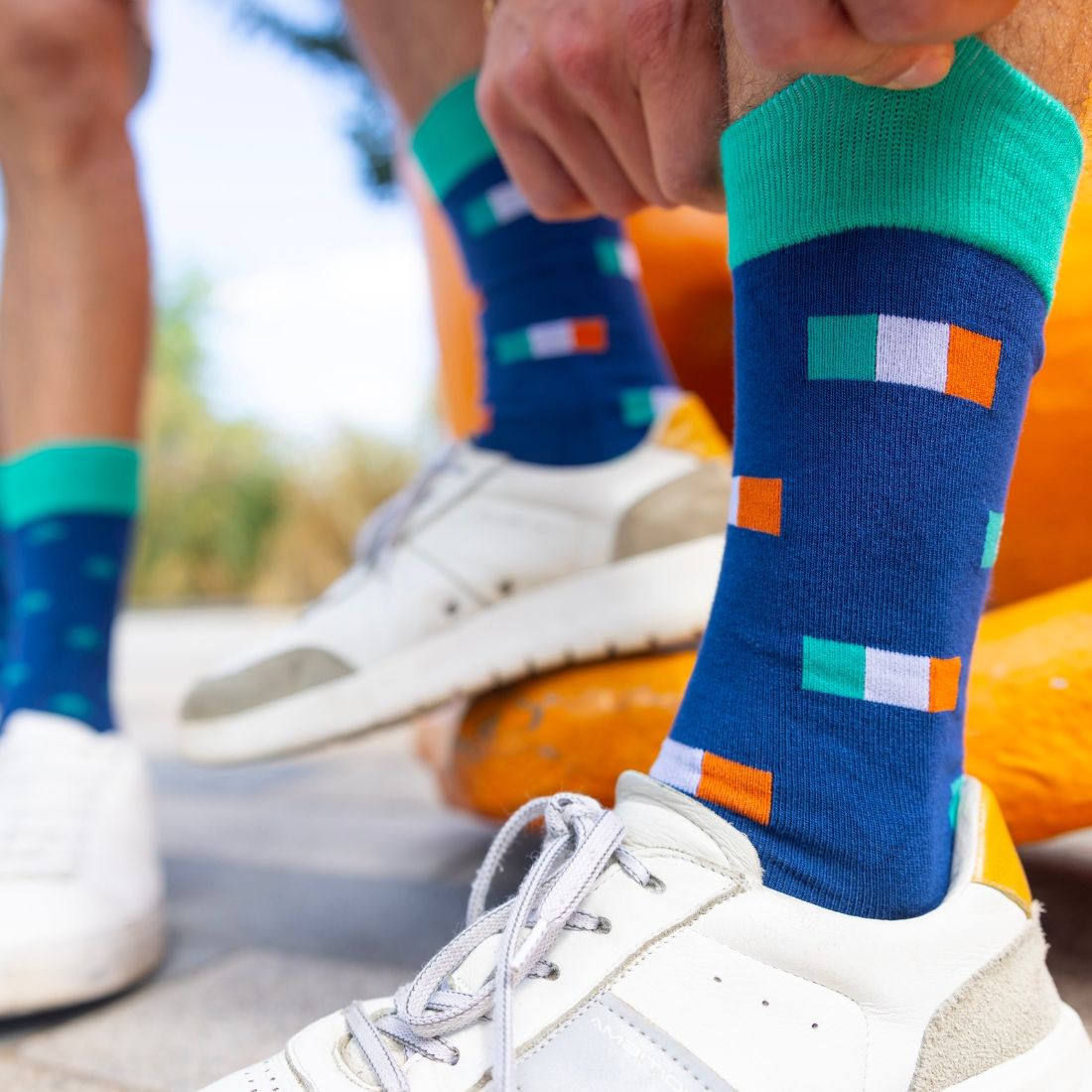 Close-up of feet wearing colorful socks with Irish flag patterns, standing on a wooden surface.