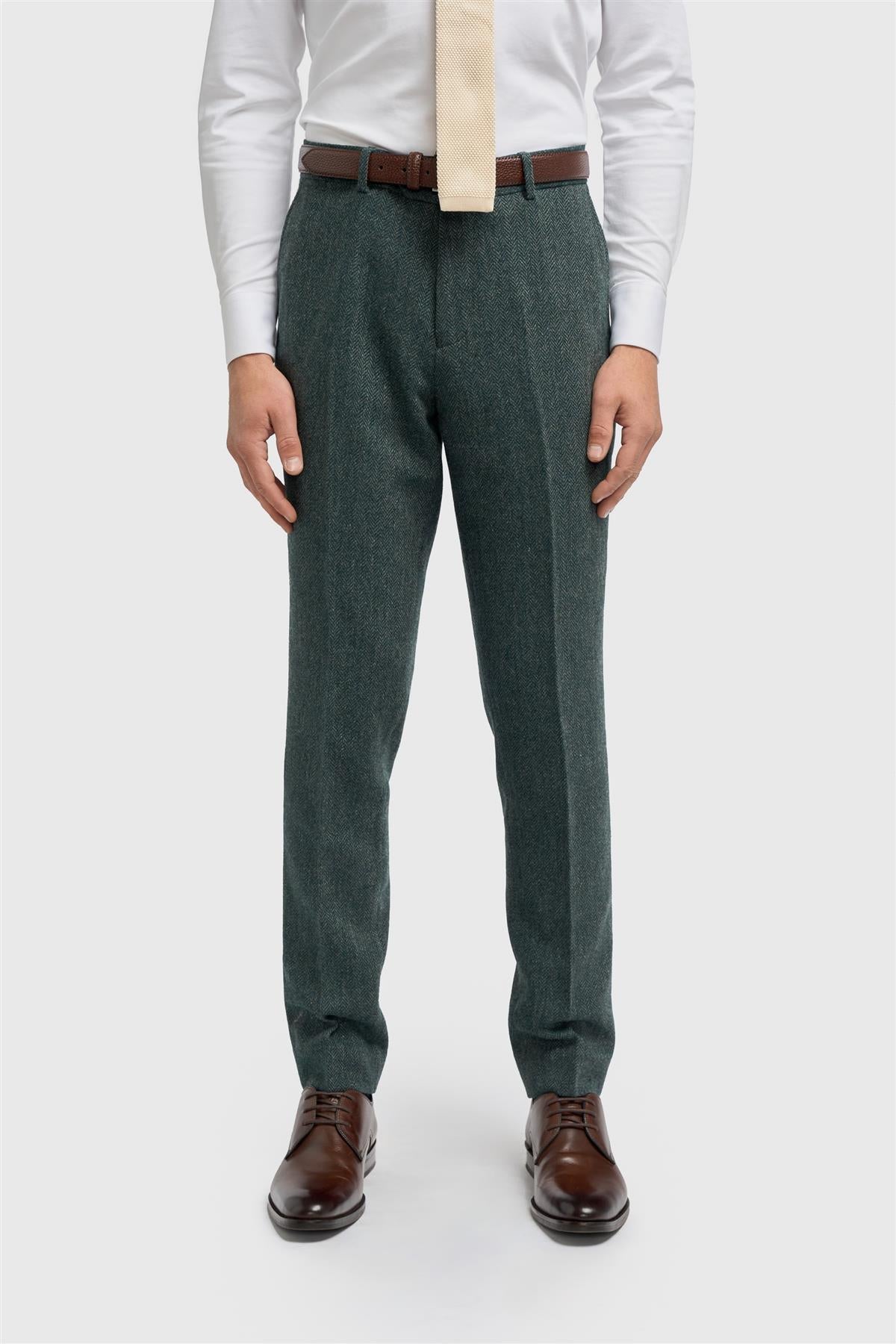 Person wearing green dress pants with a white shirt and brown shoes on a light gray background