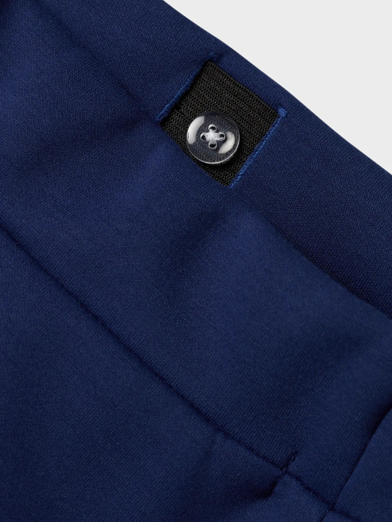 Close-up of a blue fabric pant with a button adjuster on the waistband on a white background