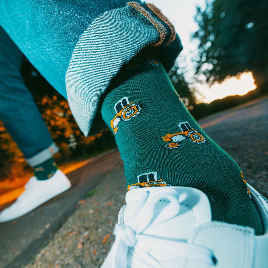 Green socks with tractor design worn with white sneakers on a blurred outdoor background
