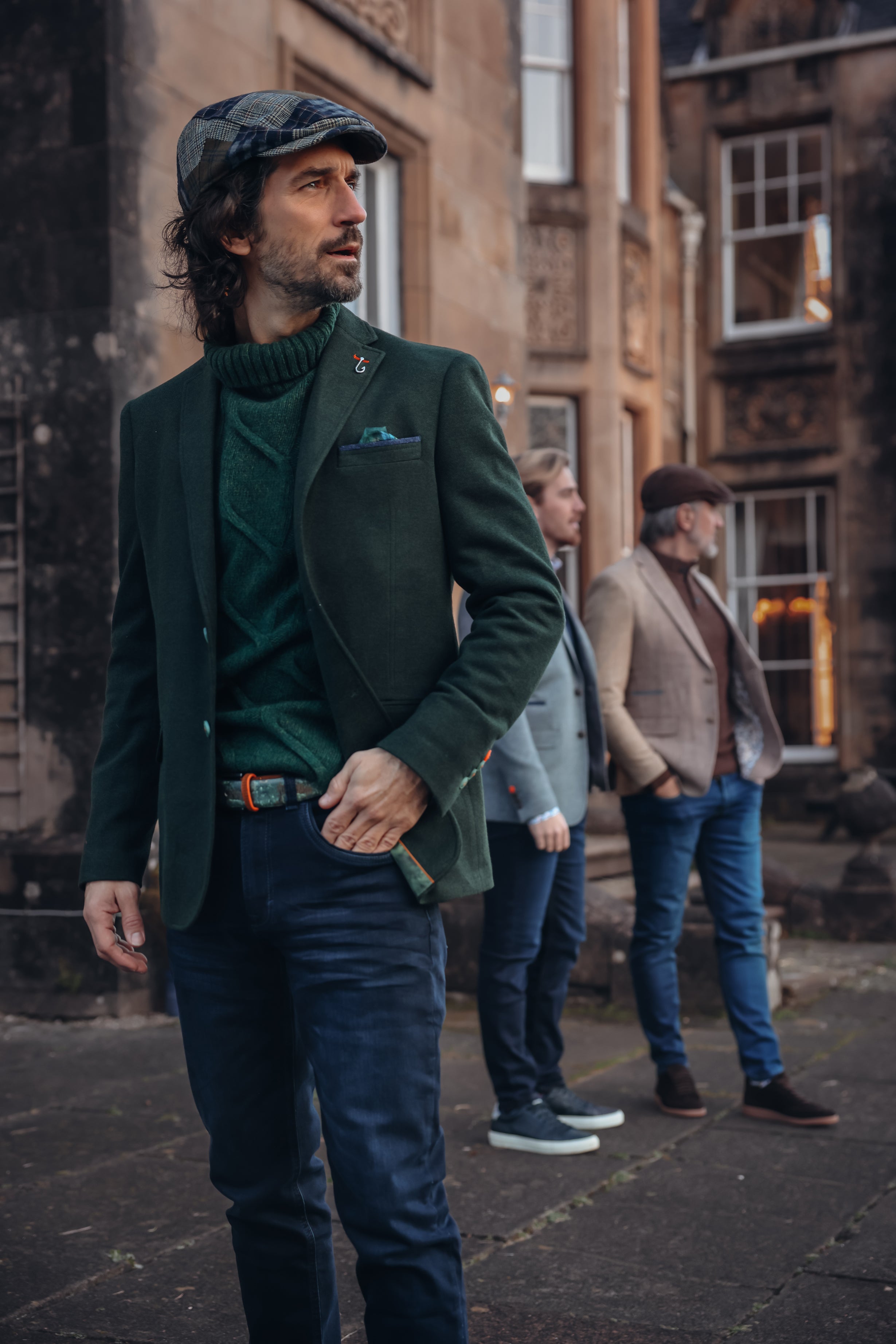 Man in a green jacket and cap standing on a street with other people in the background