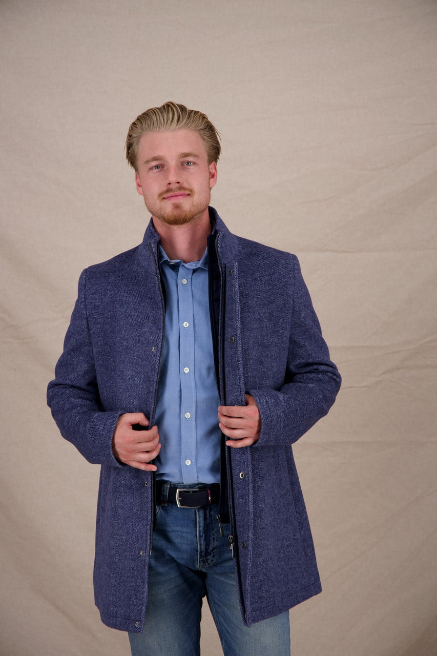Man wearing a blue coat over a light blue shirt and jeans on a beige background