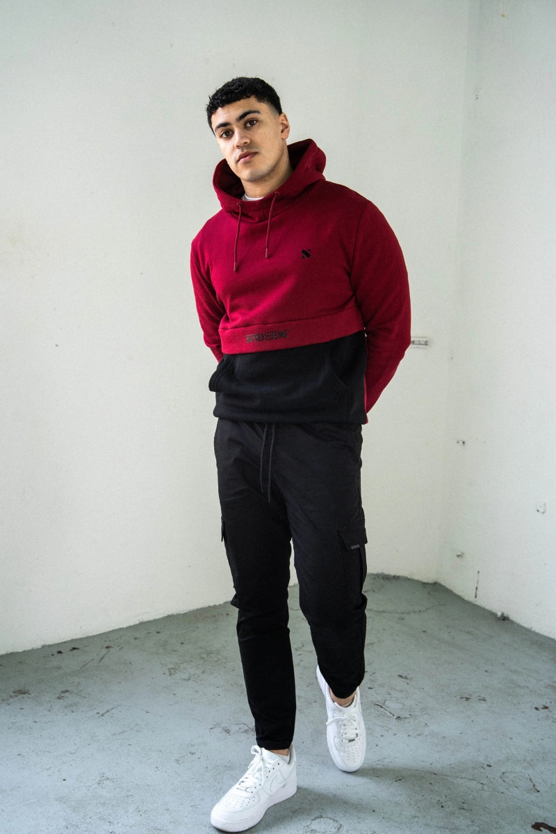 Person wearing a red hoodie and black pants standing against a white wall.