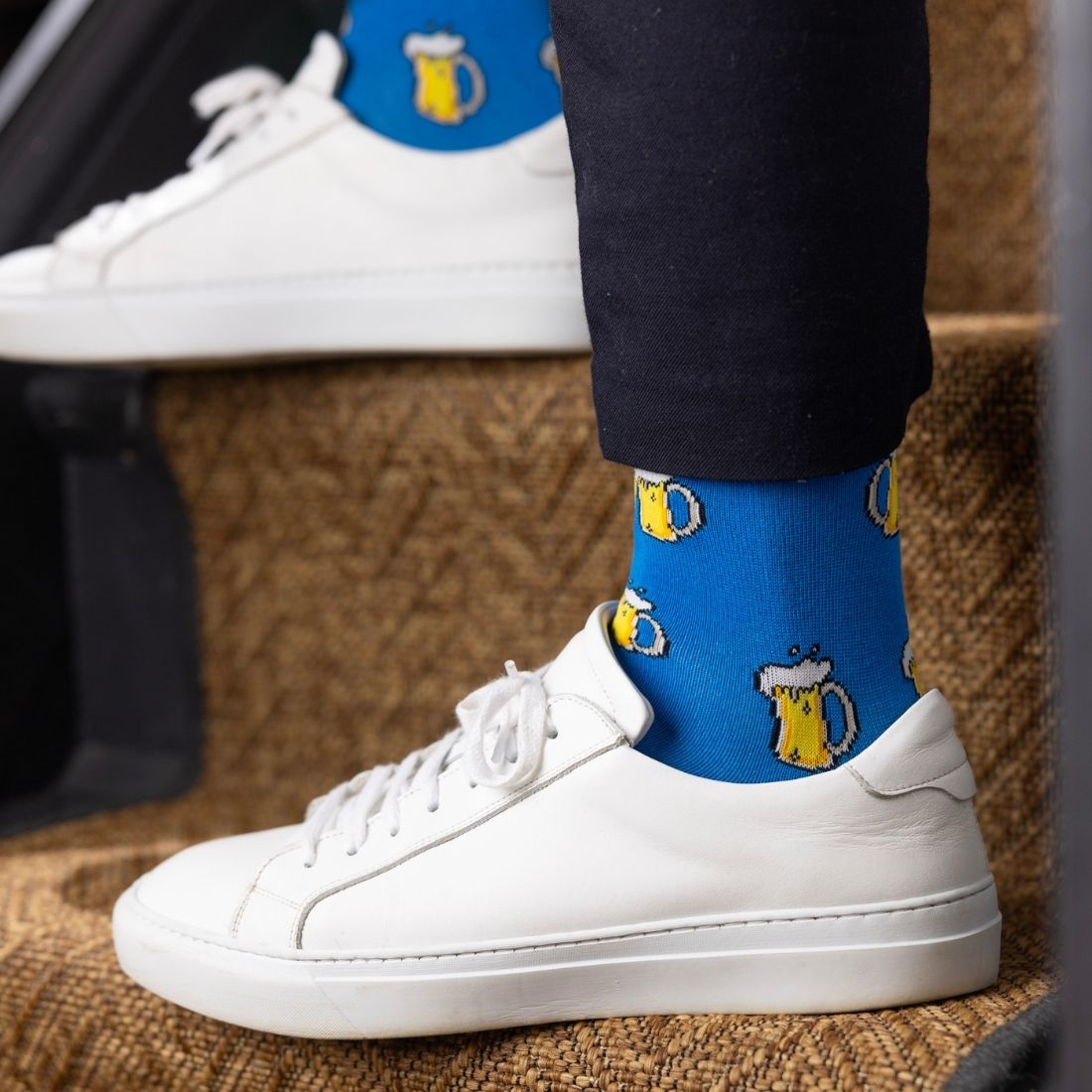 White sneakers with blue socks featuring beer mug designs on a textured surface.