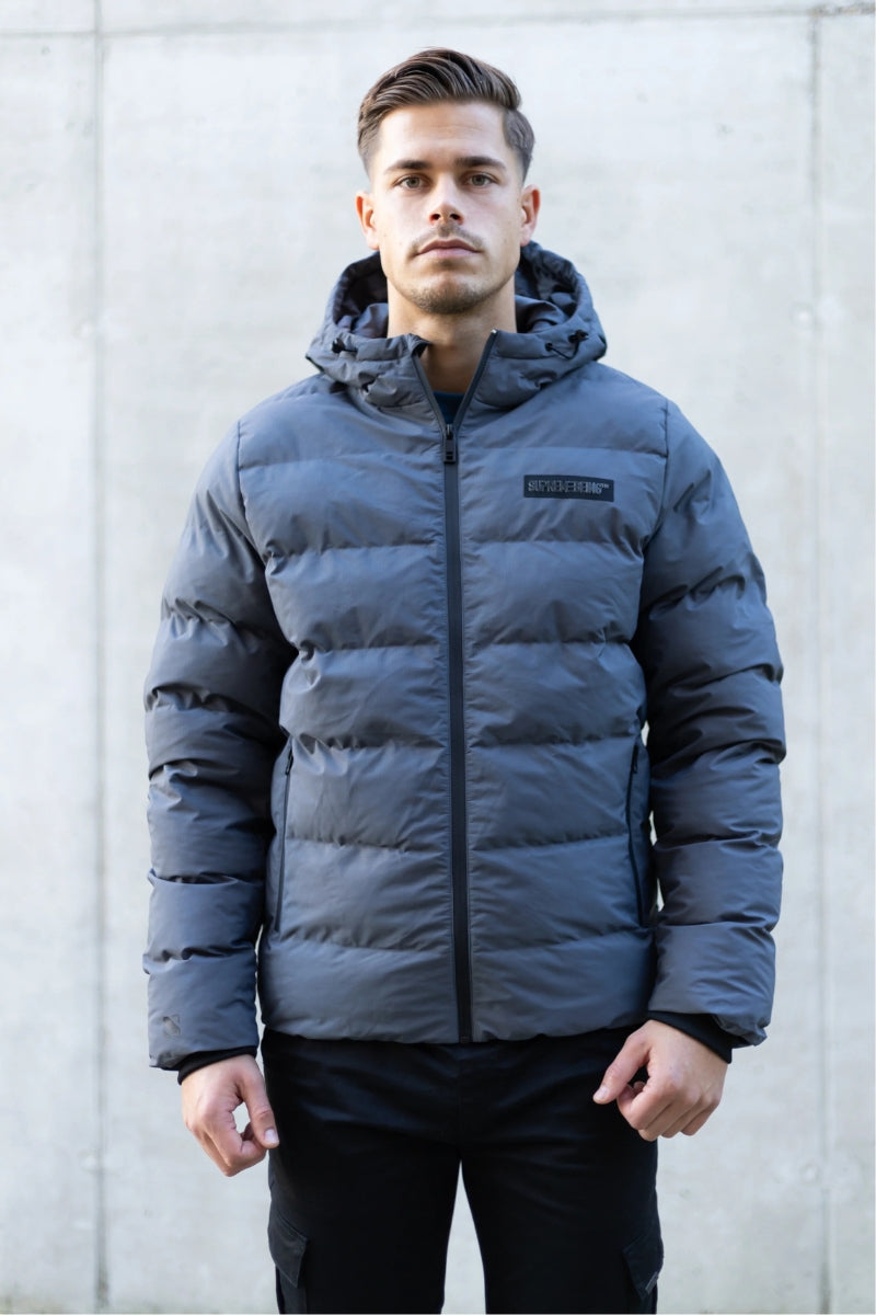 Man wearing a blue puffer jacket with a brand logo against a light gray background