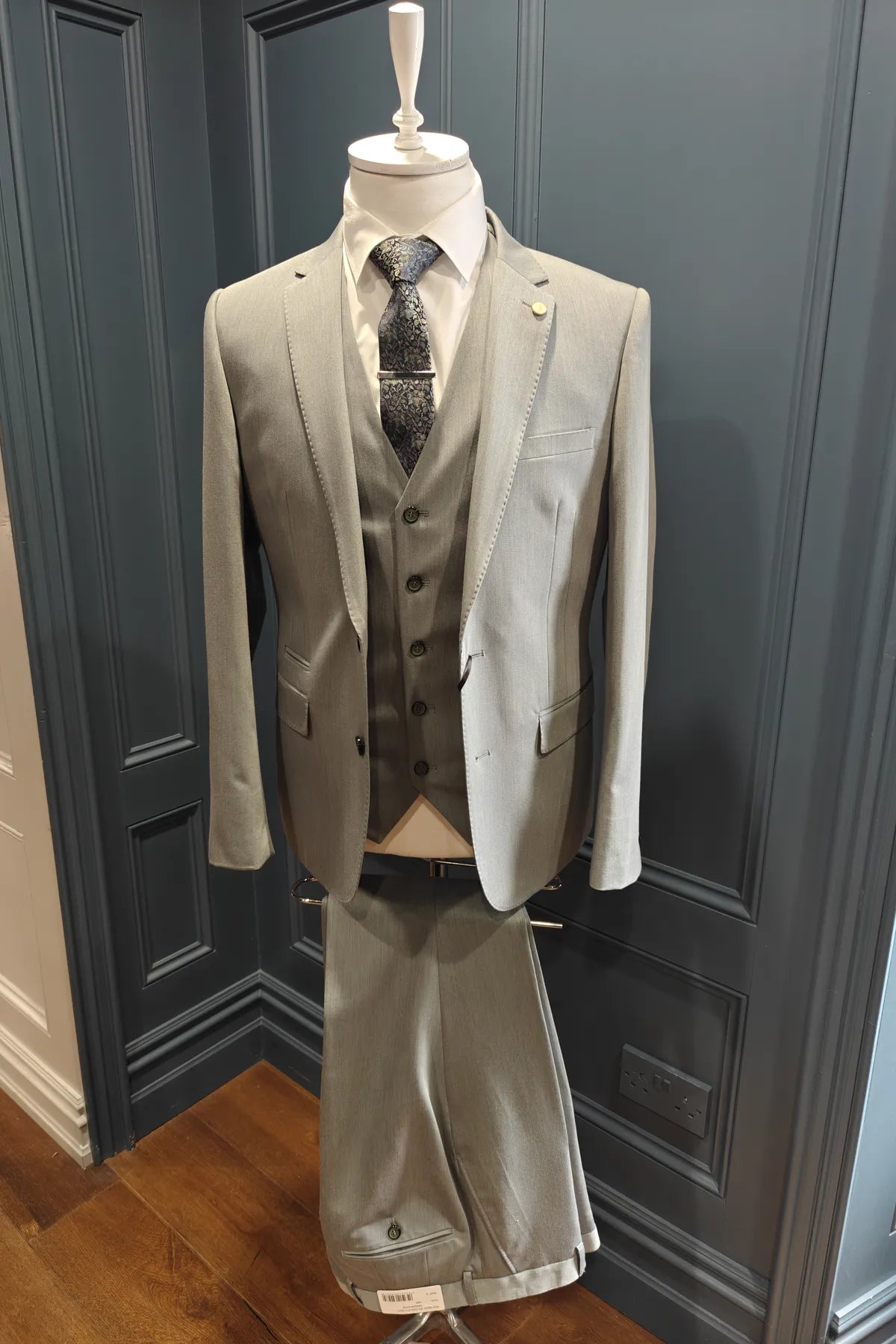 Windsor shade green 3 piece suit on a mannequin against a dark paneled wall.