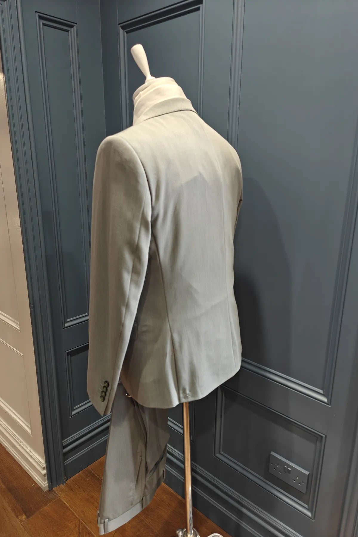 Windsor shade green 3 piece suit on a mannequin against a gray paneled wall. Back view