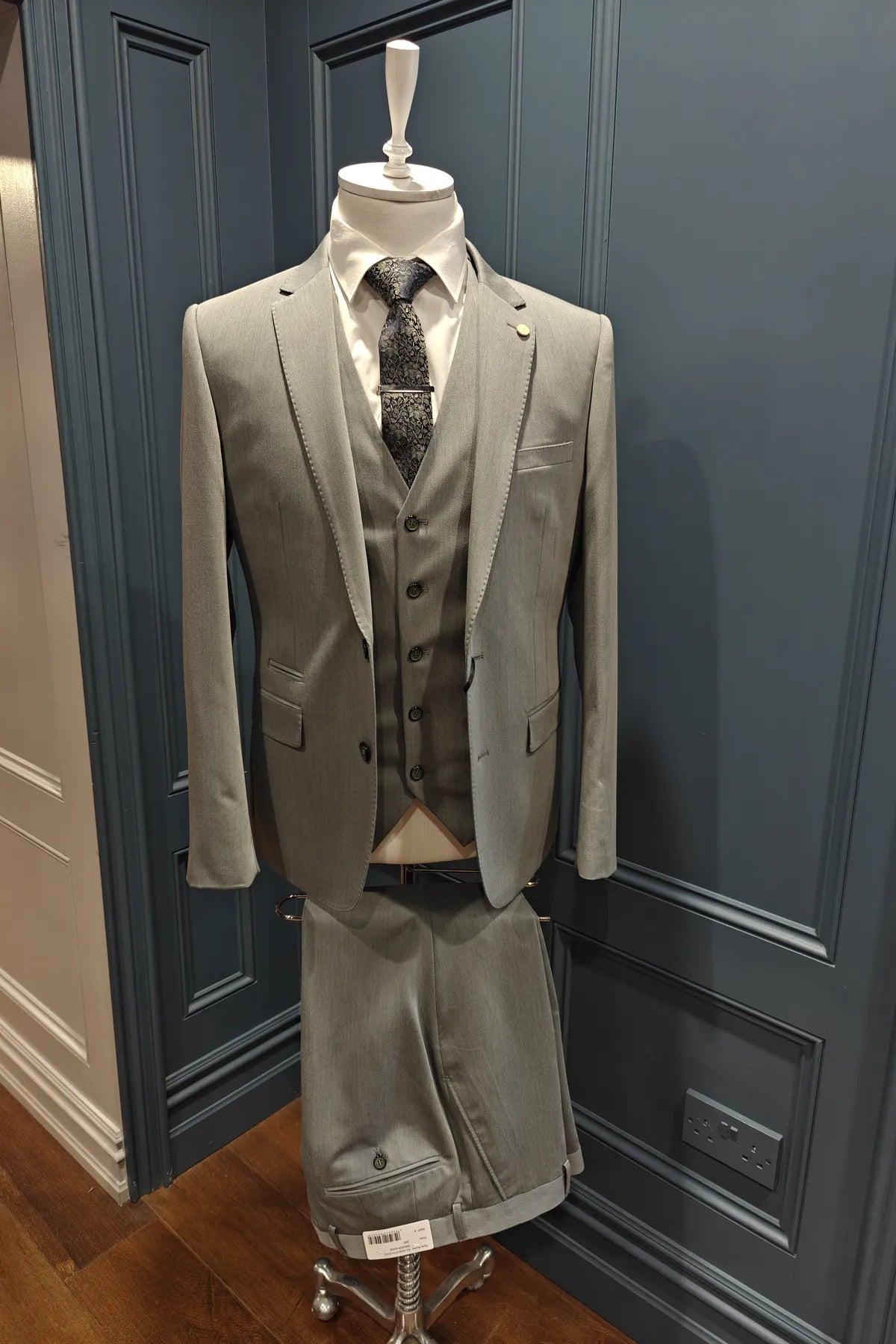Windsor shade green 3 piece suit on a mannequin against a blue paneled wall
