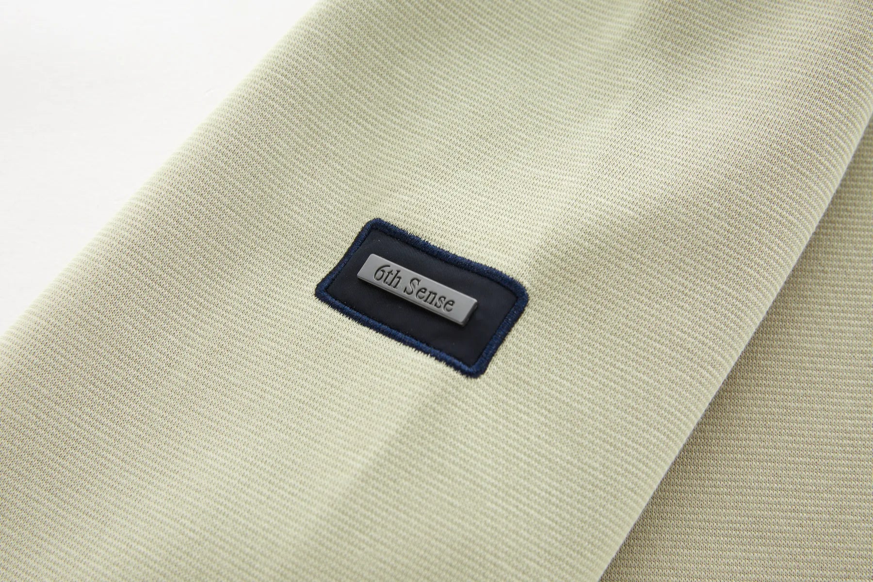 Close-up of a beige fabric with a '6th Sense' label on a white background