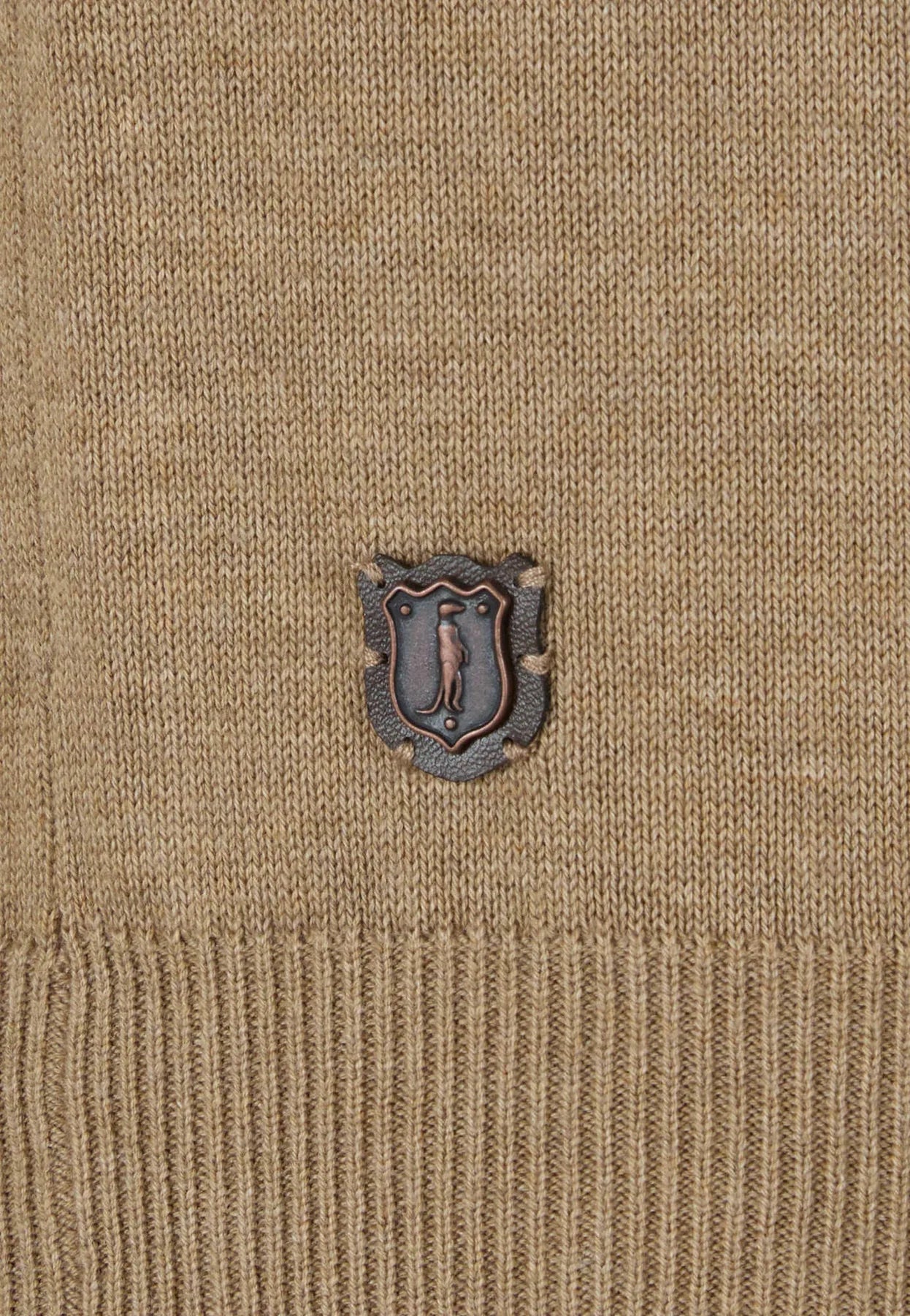 Close-up of a beige sweater with a small embroidered logo on a textured background