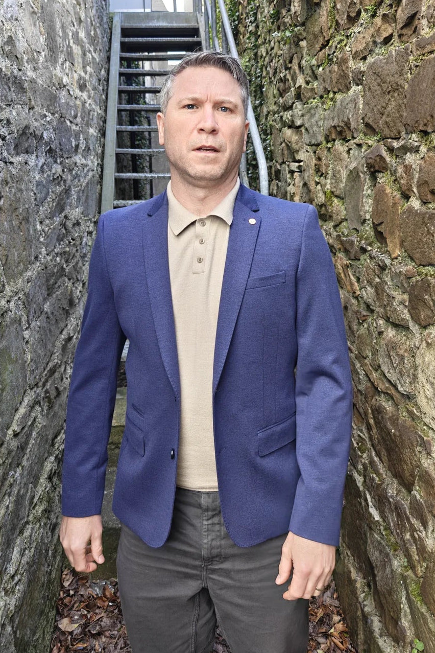 Man in a denim blue blazer standing between two stone walls