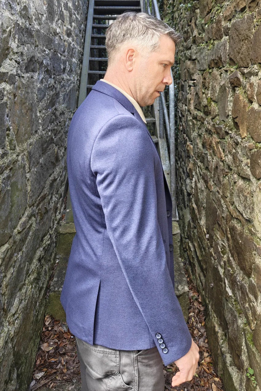 Man in a blue blazer jacket standing in a narrow stone alleyway.