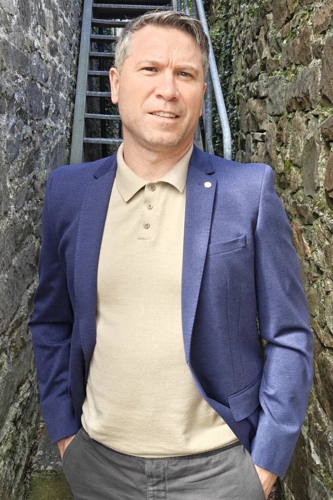 Man in a blue blazer standing in a narrow stone alleyway with stone walls and a metal staircase.