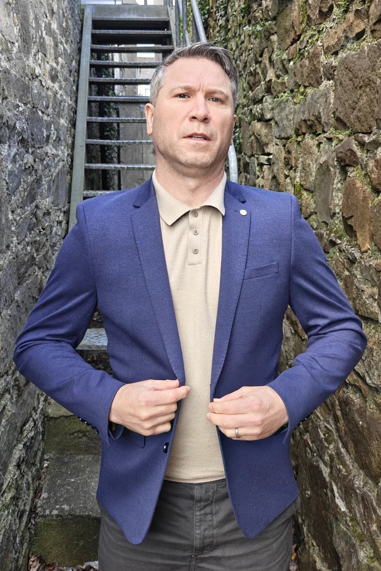 Man in a blue blazer standing between stone walls with a staircase in the background