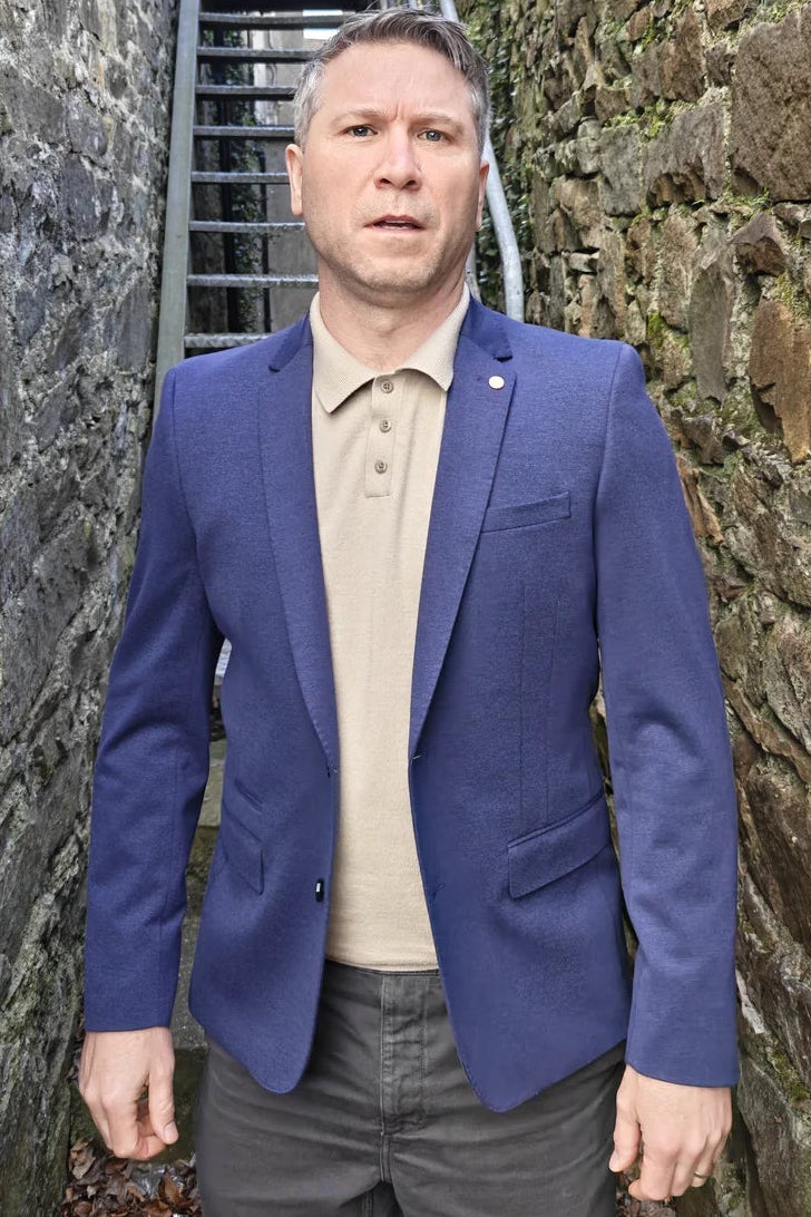 Man in a blue blazer standing between stone walls with a staircase in the background.