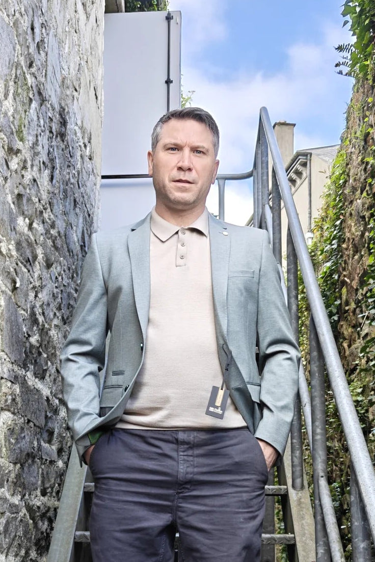 Man standing on a stone staircase between two stone walls in a pale olive blazer