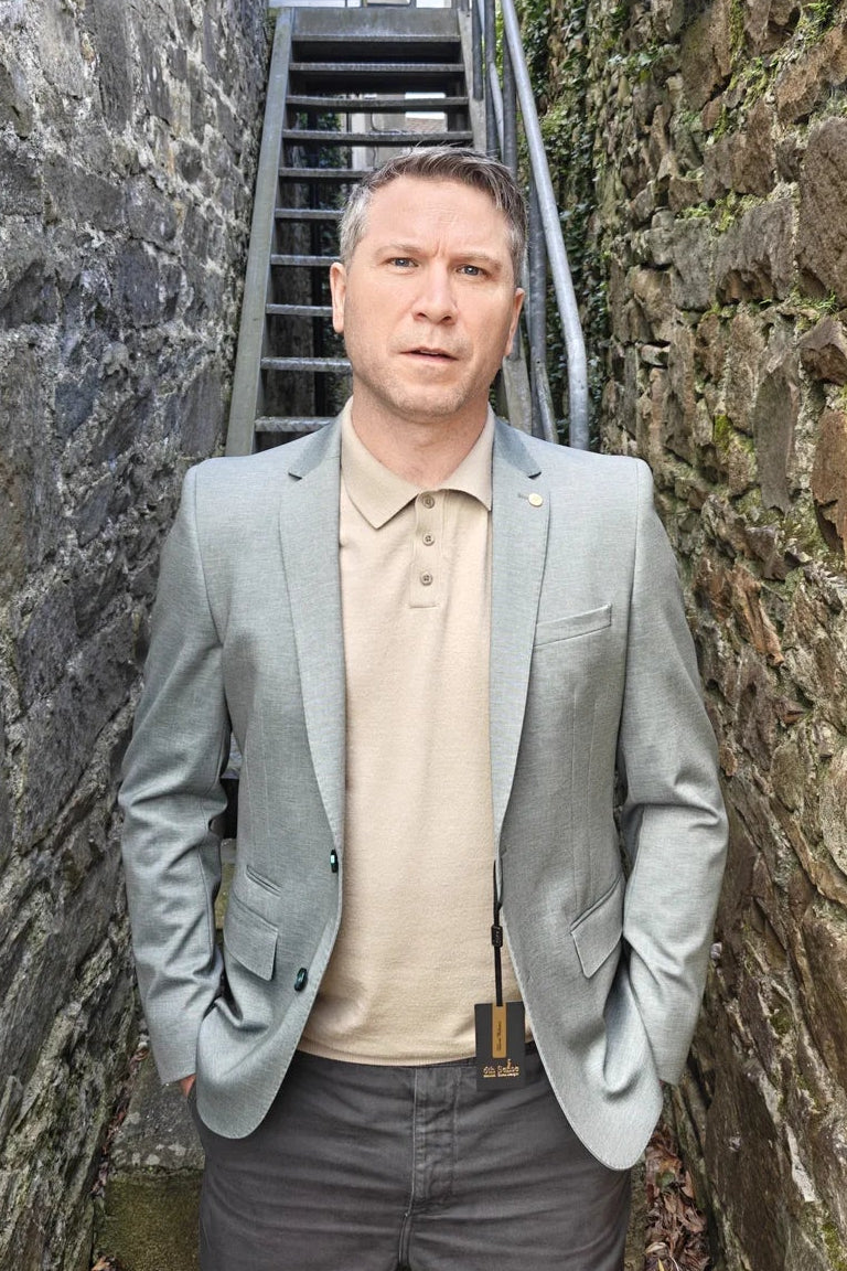 Man in a pale olive blazer standing between stone walls with a staircase in the background