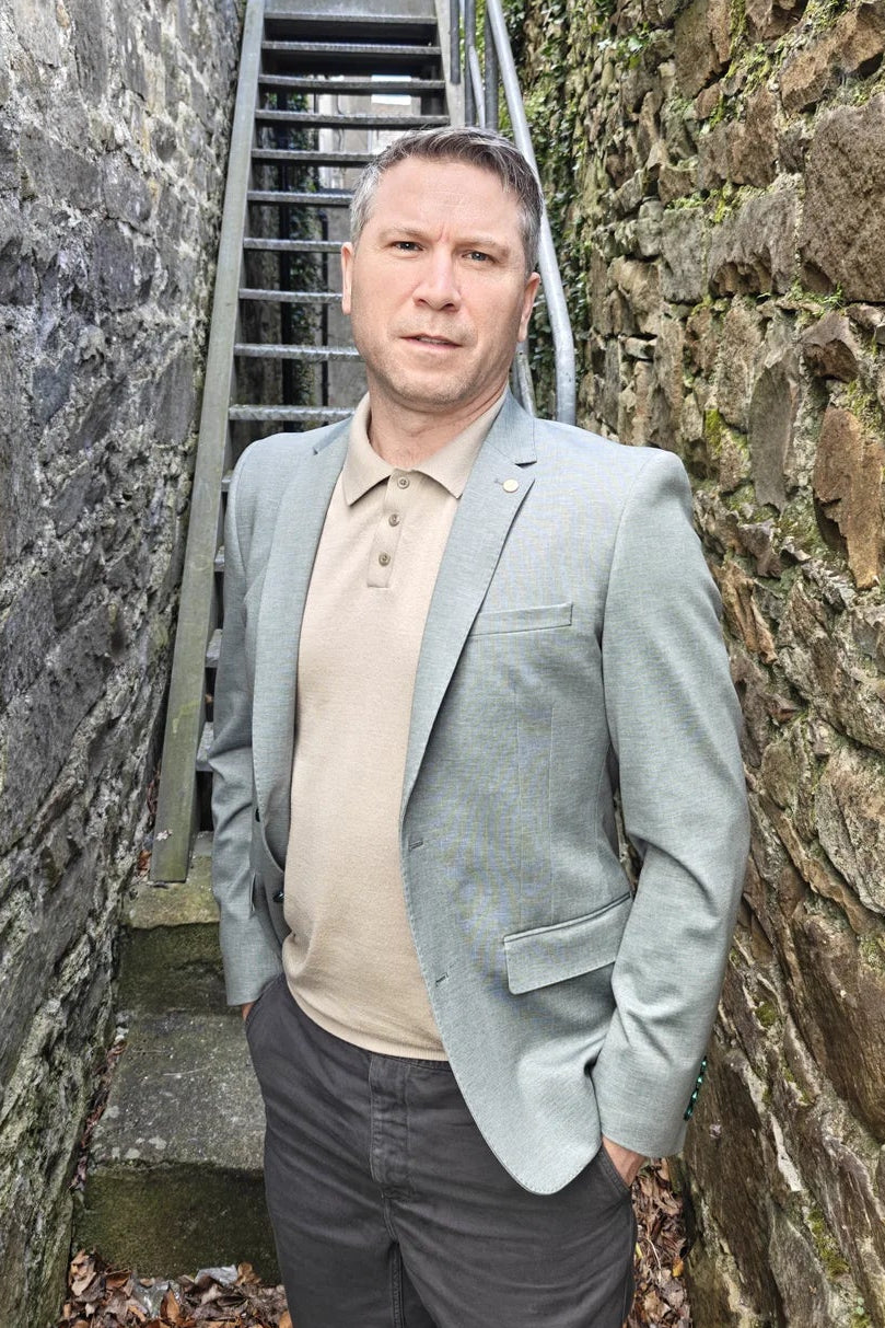 Man standing in a narrow stone alleyway with a staircase in a pale olive blazer