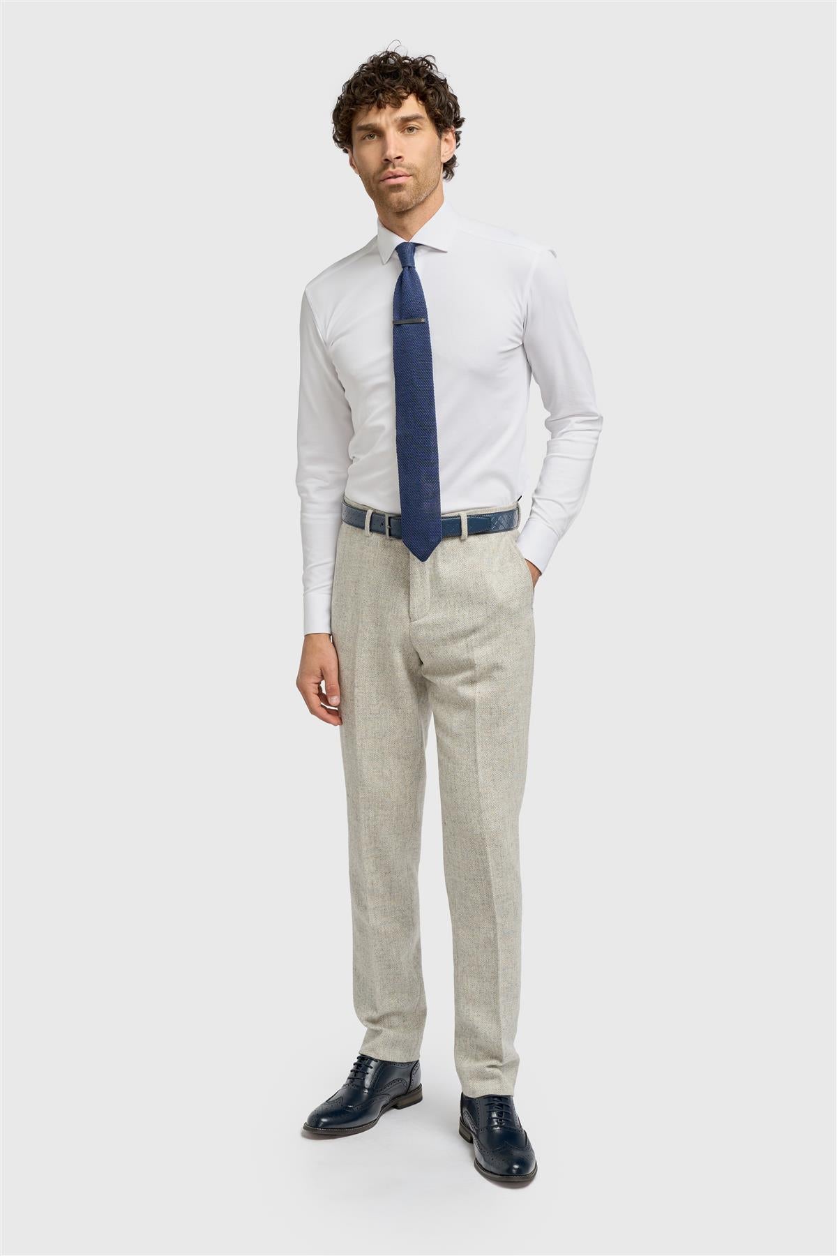 Man wearing a white dress shirt, blue tie, beige pants, and black shoes on a light gray background