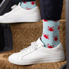 White sneakers with light blue socks featuring red crab patterns on a textured surface.