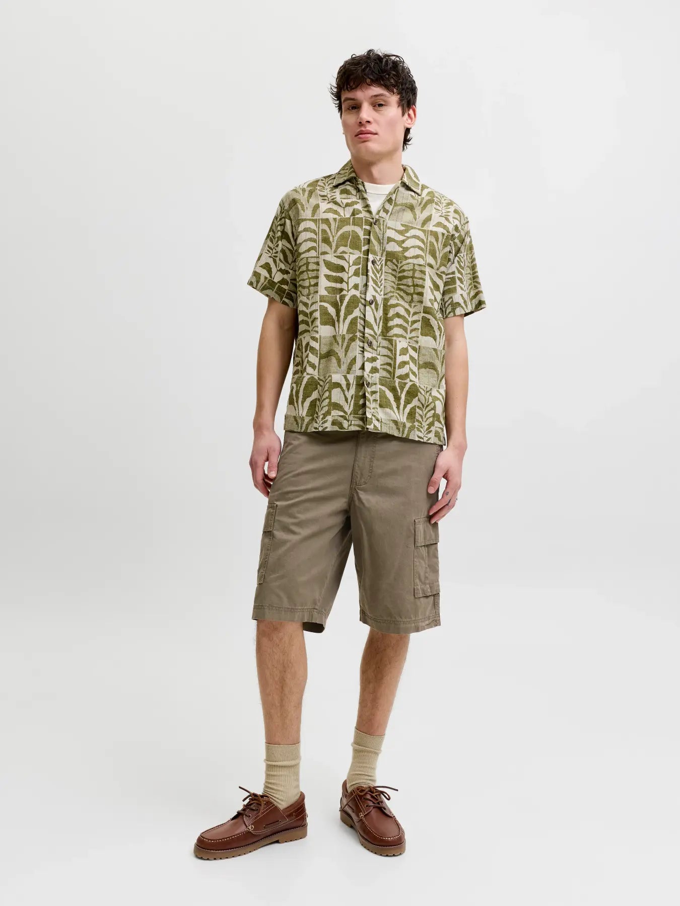 Person wearing a patterned shirt, cargo shorts, and brown shoes on a white background