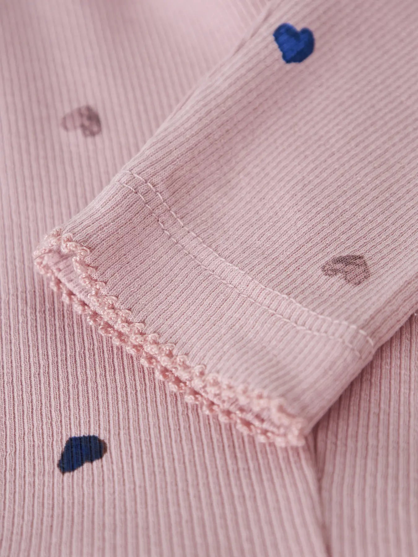 Close-up of a pink textured fabric with embroidered heart designs.