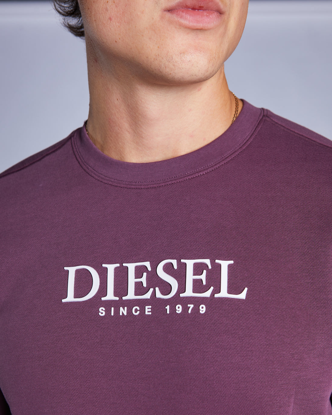 Close-up of a person wearing a purple Diesel sweatshirt with the brand logo.