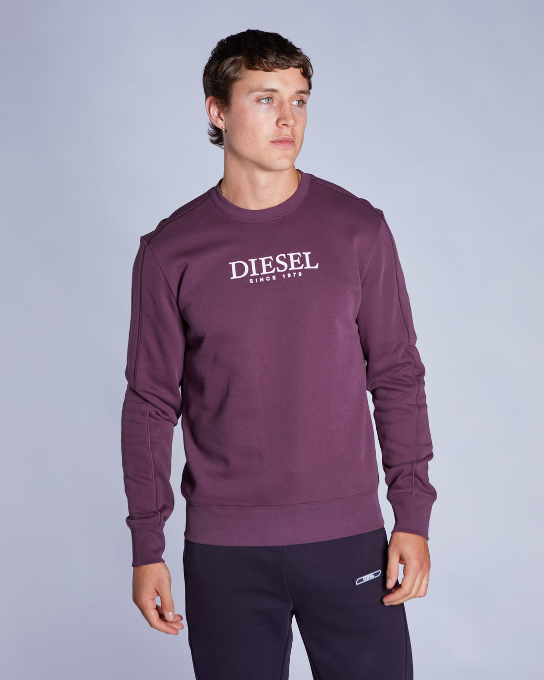Man wearing a purple Diesel sweatshirt against a gray background