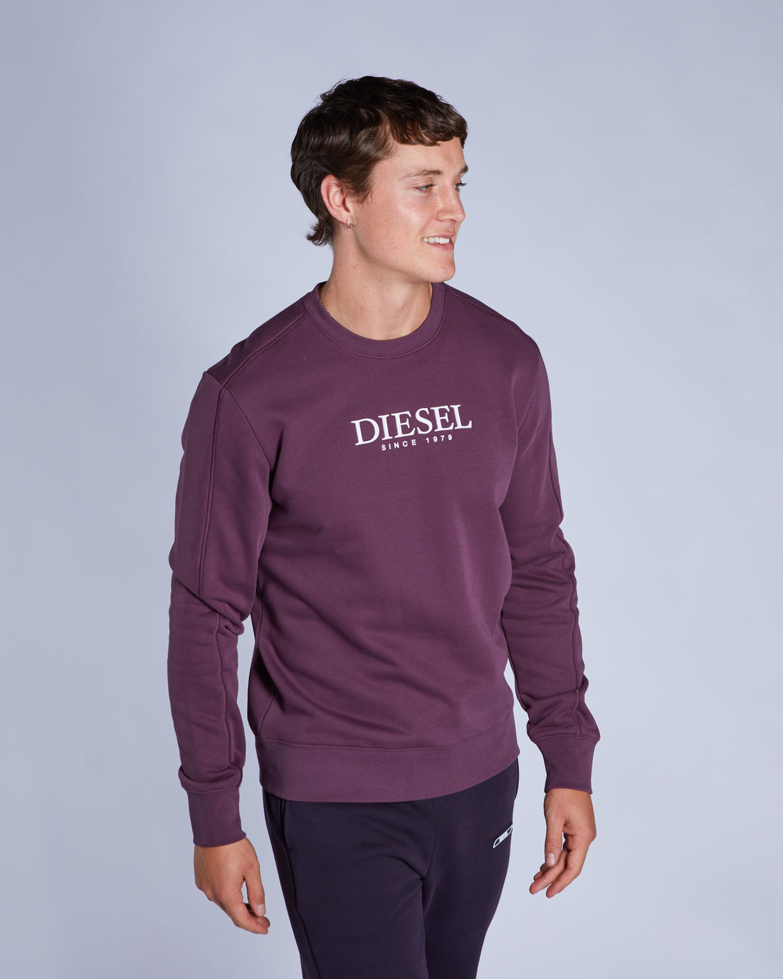 Man wearing a purple Diesel sweatshirt against a light gray background