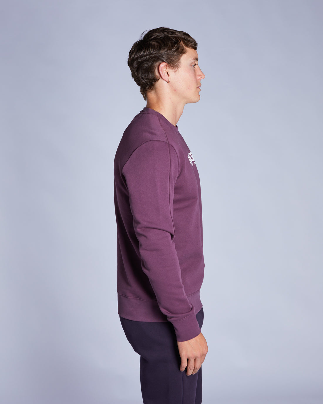 Person wearing a purple sweatshirt with a logo on a gray background