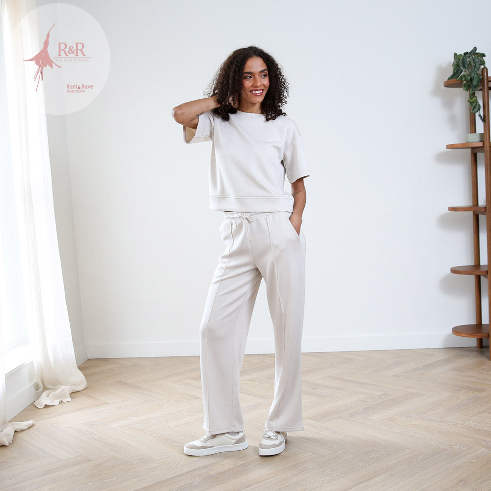 Woman wearing a white outfit standing in a room with a wooden floor and white walls.
