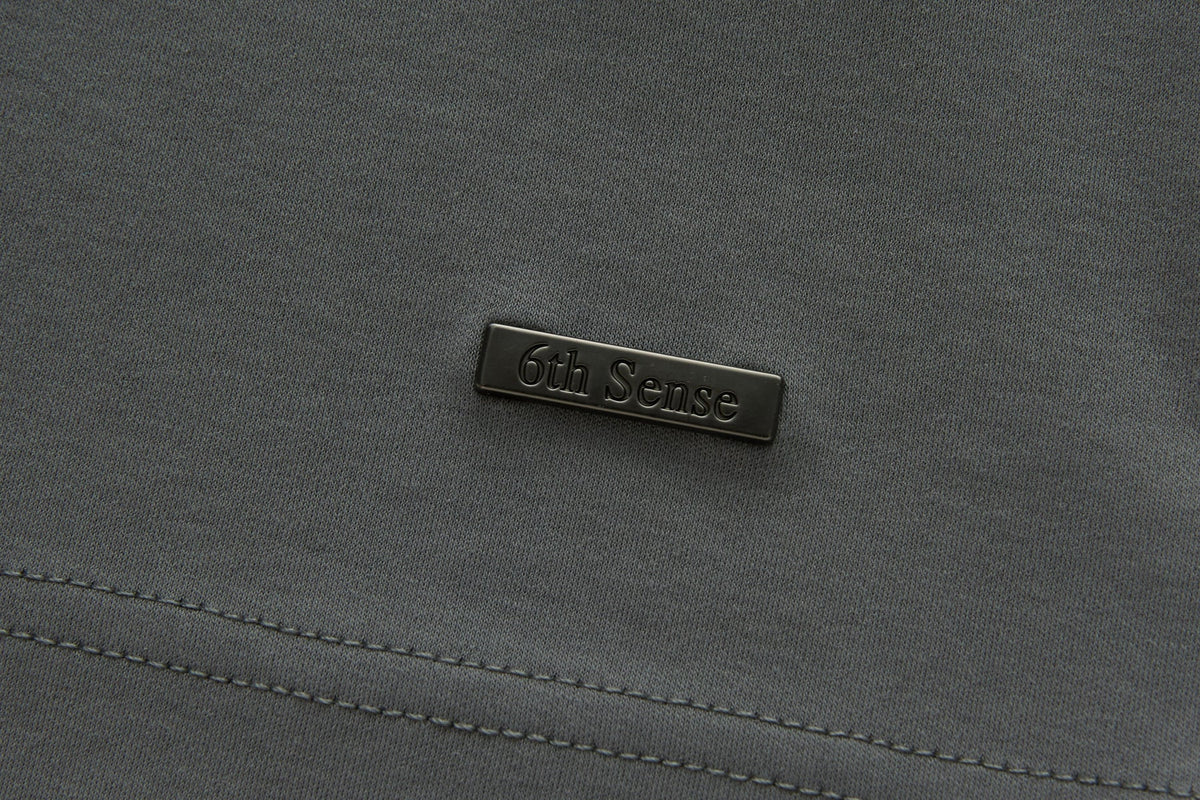 Close-up of the 6th Sense Astound December Polo in December showing a black rectangular rubberised 6th Sense logo badge on textured fabric above a double stitched seam.