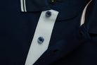 Close-up of the 6th Sense Astound Eclipse Polo placket in Eclipse, showing two dark buttons on a light placket, a striped collar tip, a small M size label, and contrast trim along the inner neckline.