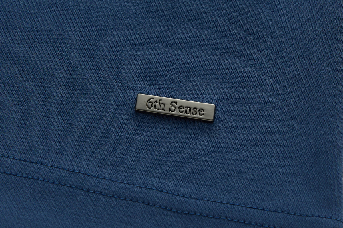 Rectangular 6th Sense metal logo badge on the lower front of the blue Astound Ensign Polo.