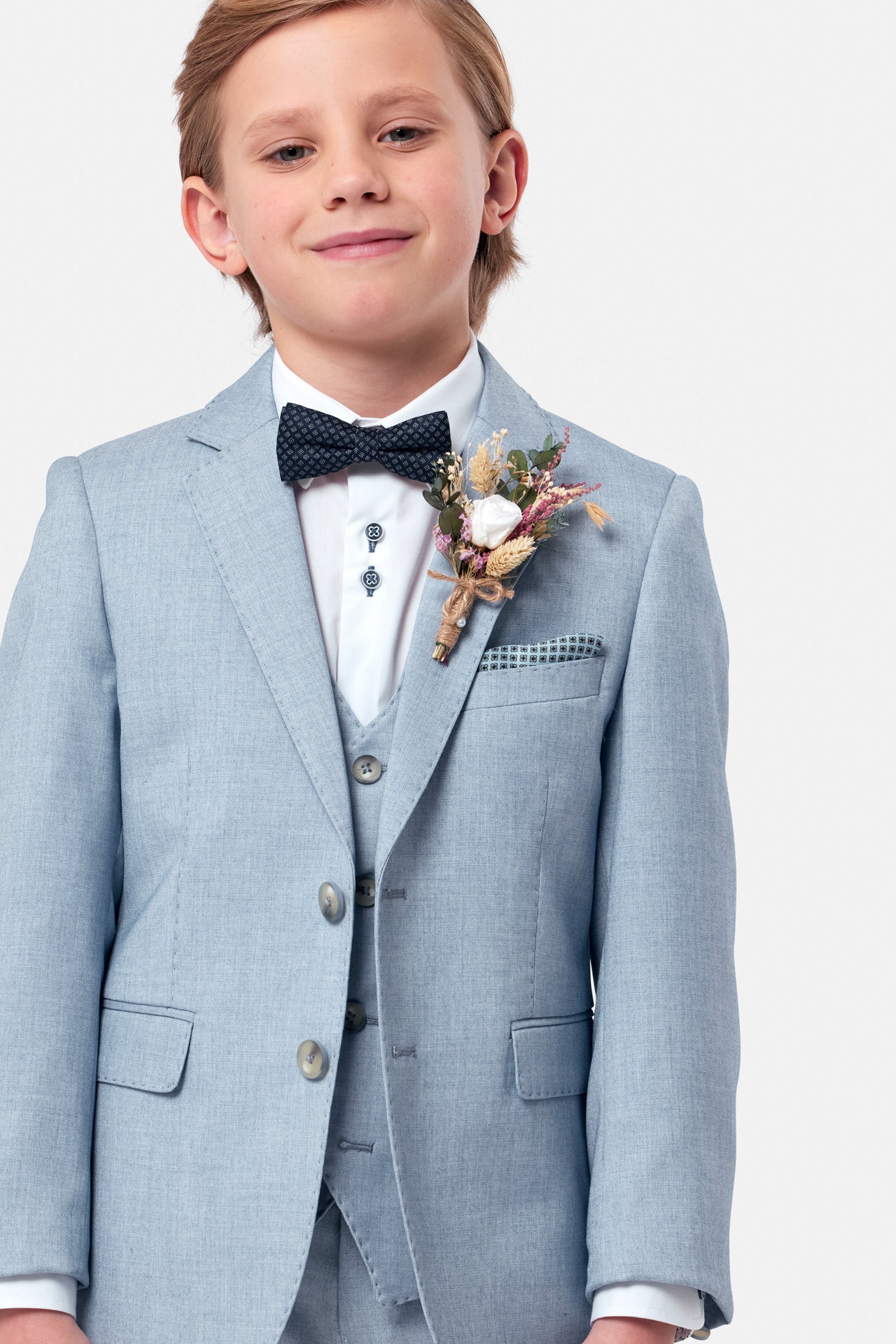 Young boy in a light blue suit with a bow tie and boutonniere on a white background