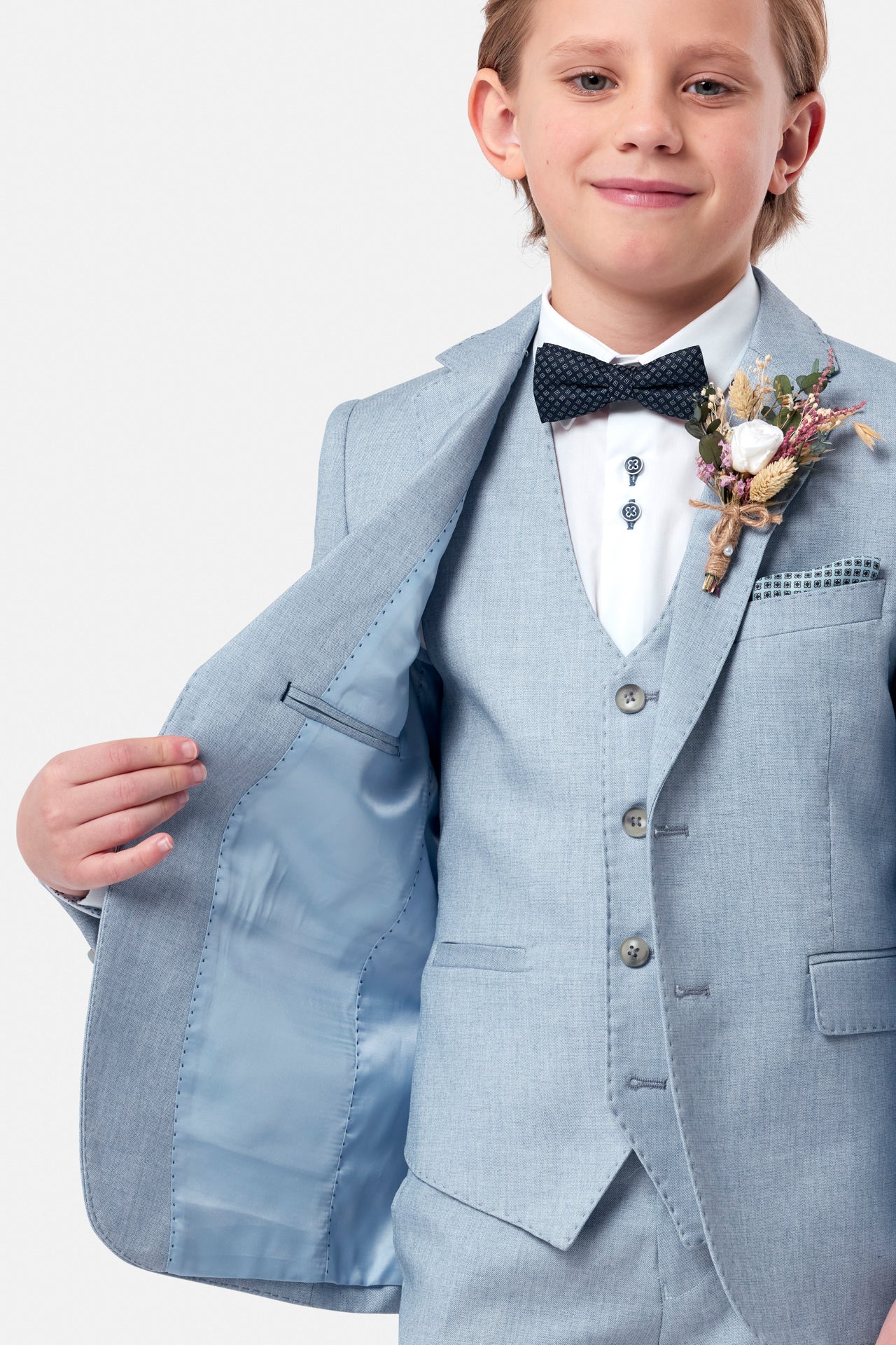 Young boy in a light blue suit with a navy bow tie and floral boutonniere on a white background