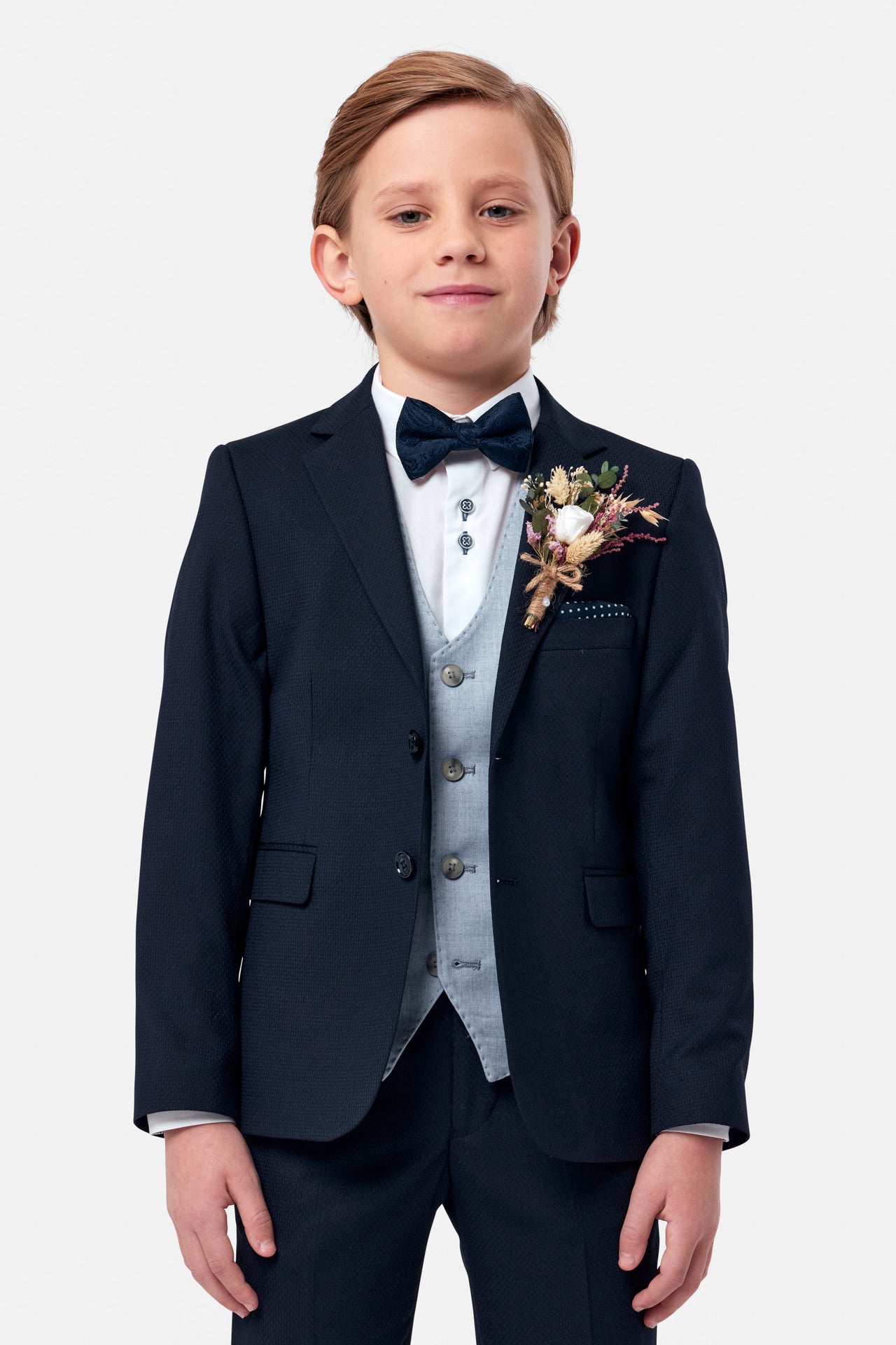 Young boy in a formal navy suit with blue waistcoat, bow tie and boutonniere on a white background