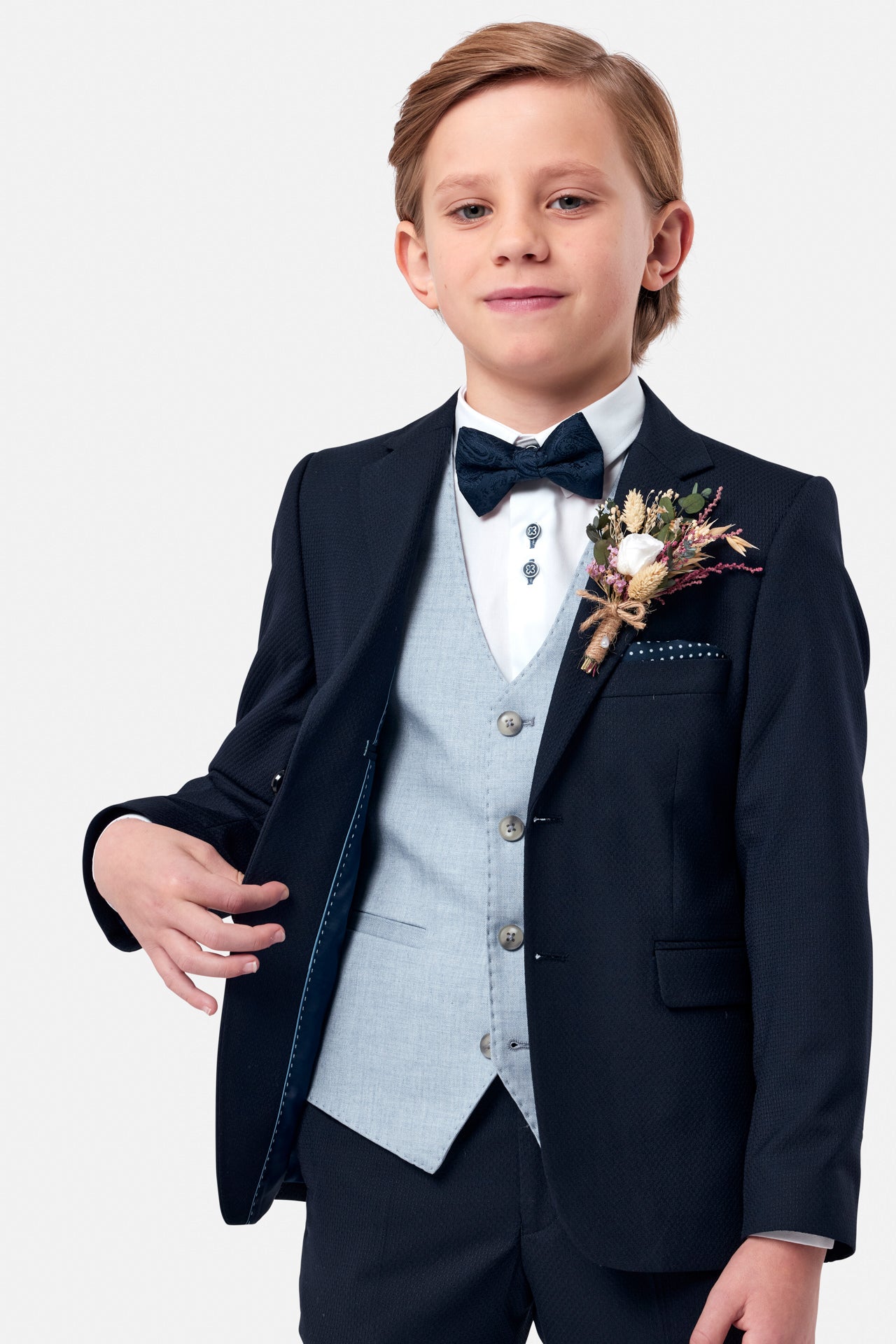 Young boy in a formal navy suit with a light blue waistcoat and bow tie, standing against a white background.