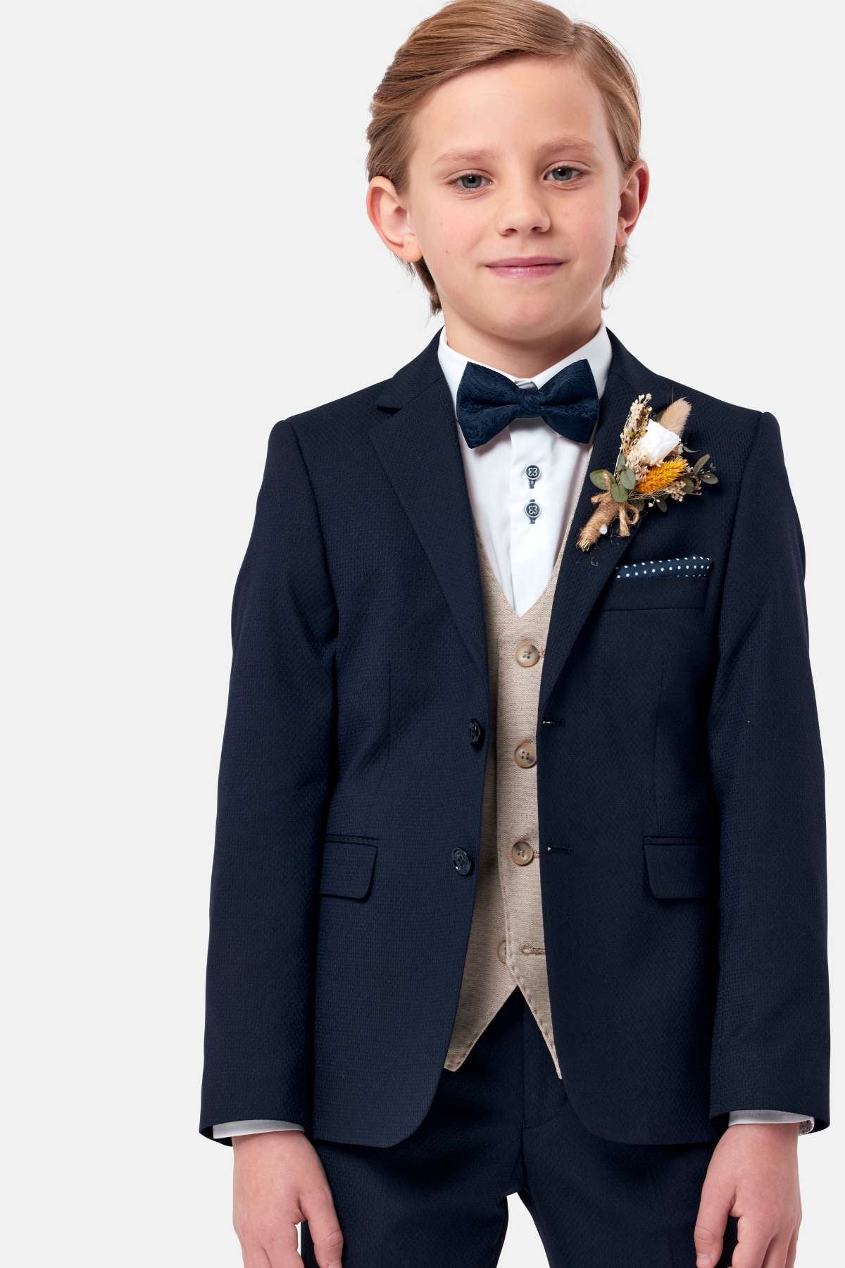 Young boy in a formal navy suit with bow tie, stone waistcoat and boutonniere on a white background