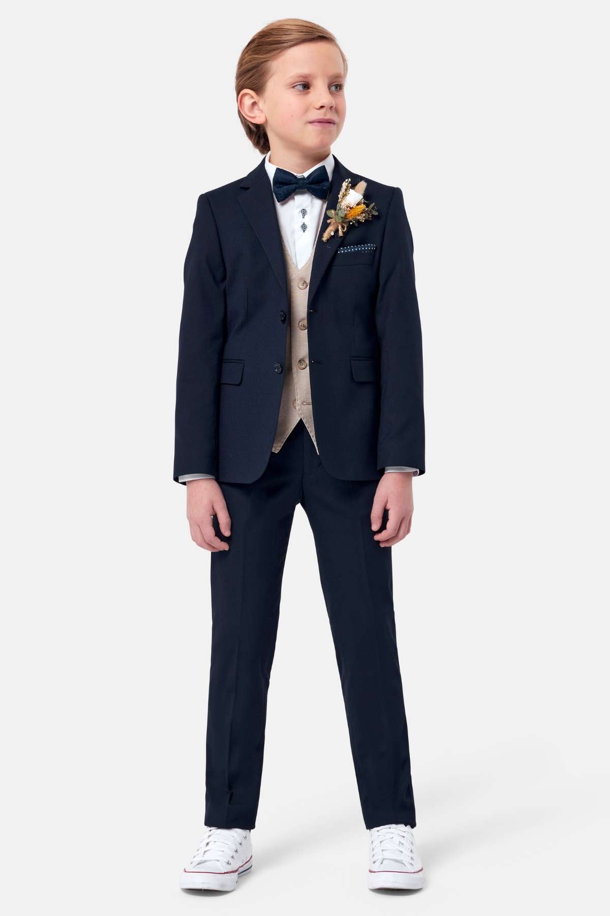 Young boy in a navy suit with a white shirt, stone waistcoat and floral boutonniere on a white background