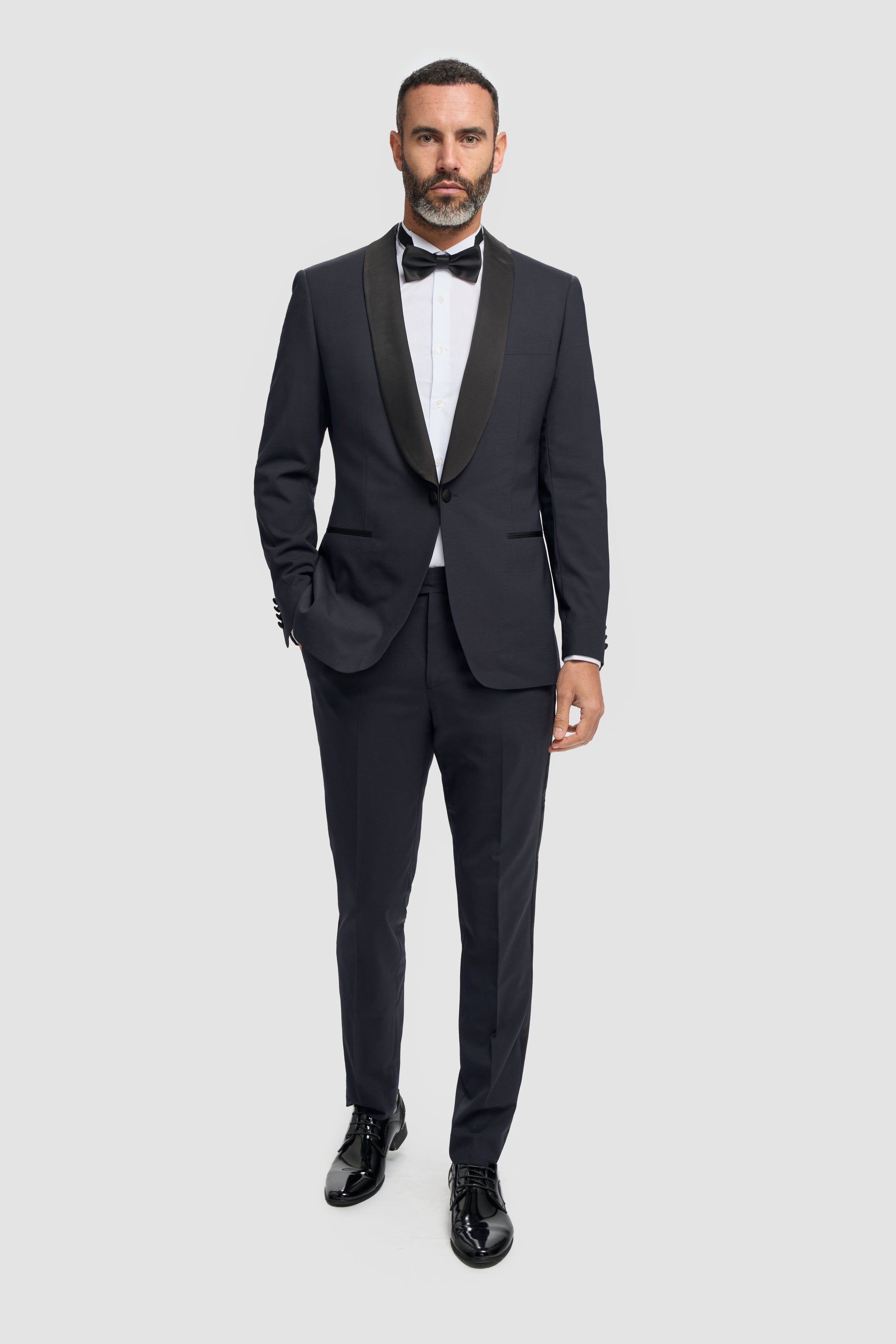 Man wearing a dark navy tuxedo with a white shirt and bow tie on a light gray background