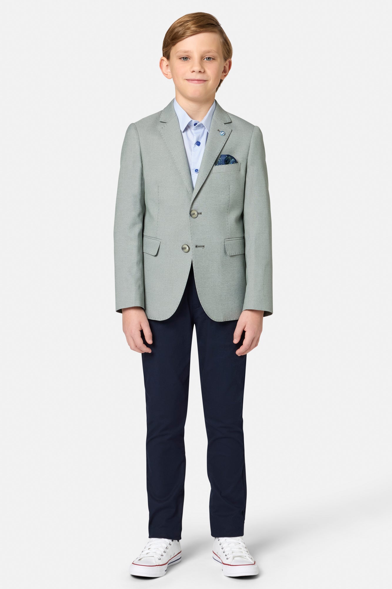 Young boy wearing a sage green blazer, navy pants, and white sneakers on a white background
