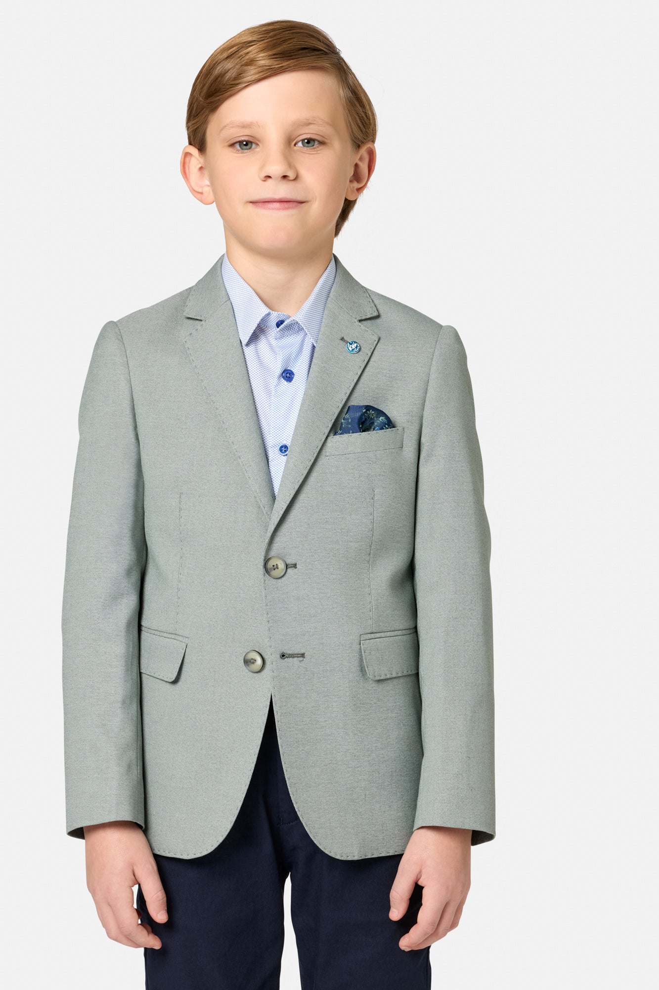 Young boy wearing a sage green blazer over a light blue shirt with a white background