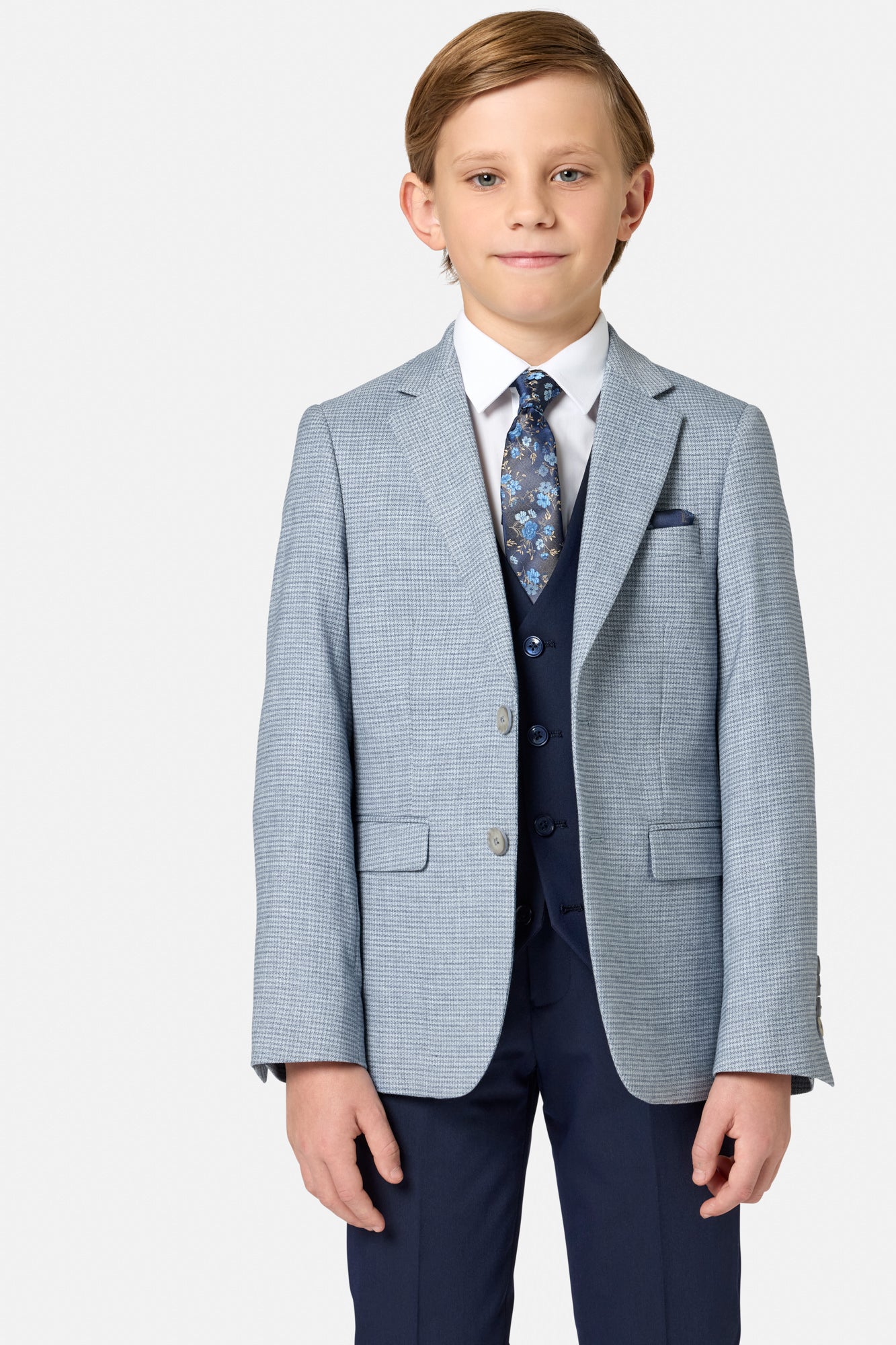 Young boy wearing a formal blue suit  jacket with a white shirt and patterned tie on a light gray background