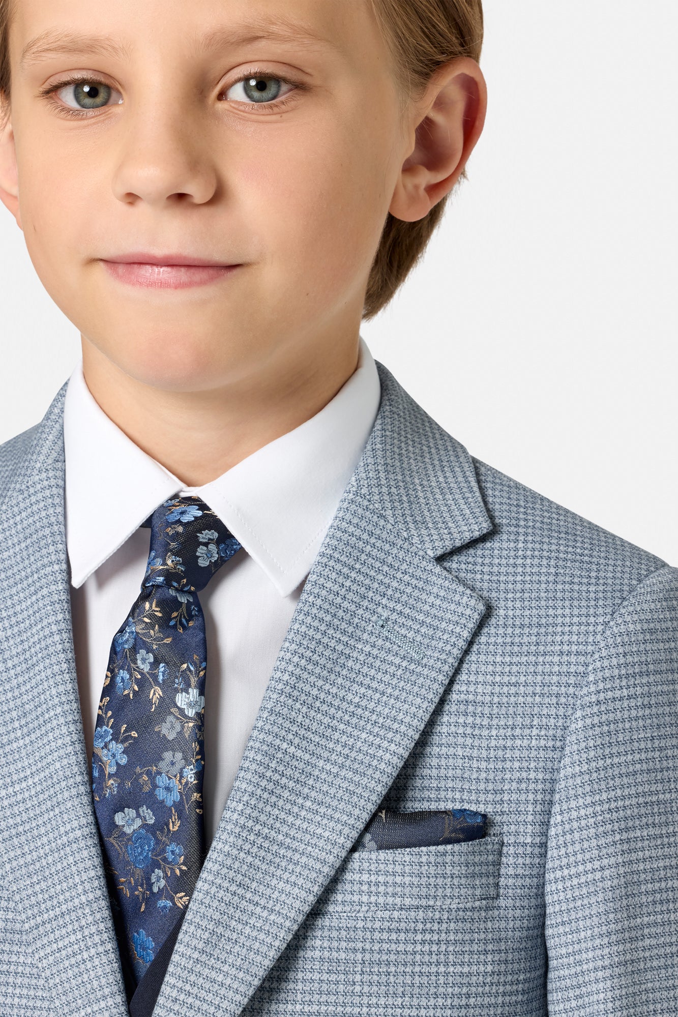 Young boy wearing a formal blue suit  jacket with a white shirt and patterned tie on a light gray background