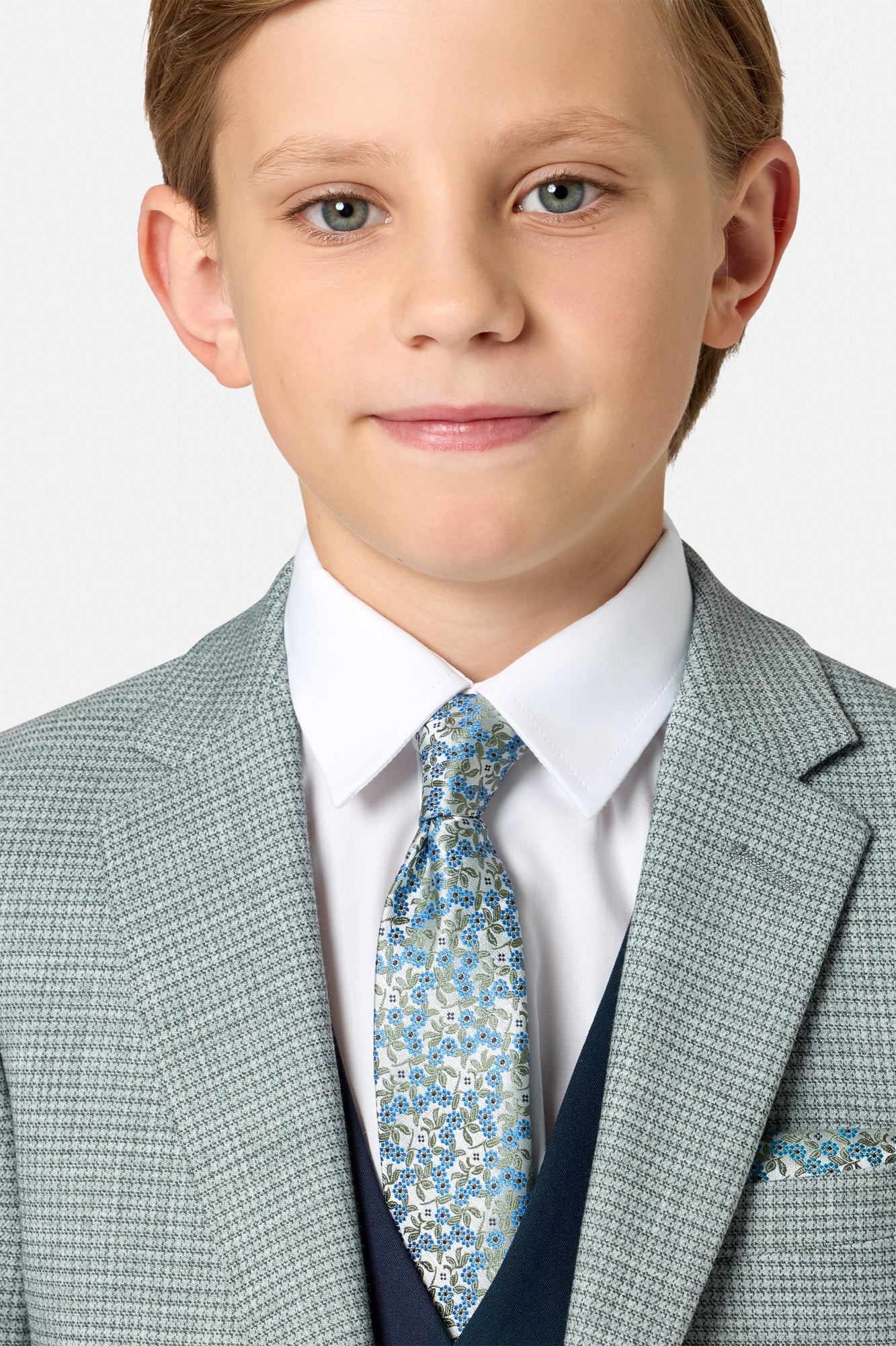 Young boy wearing a sage green checkered blazer with a blue floral tie on a white background
