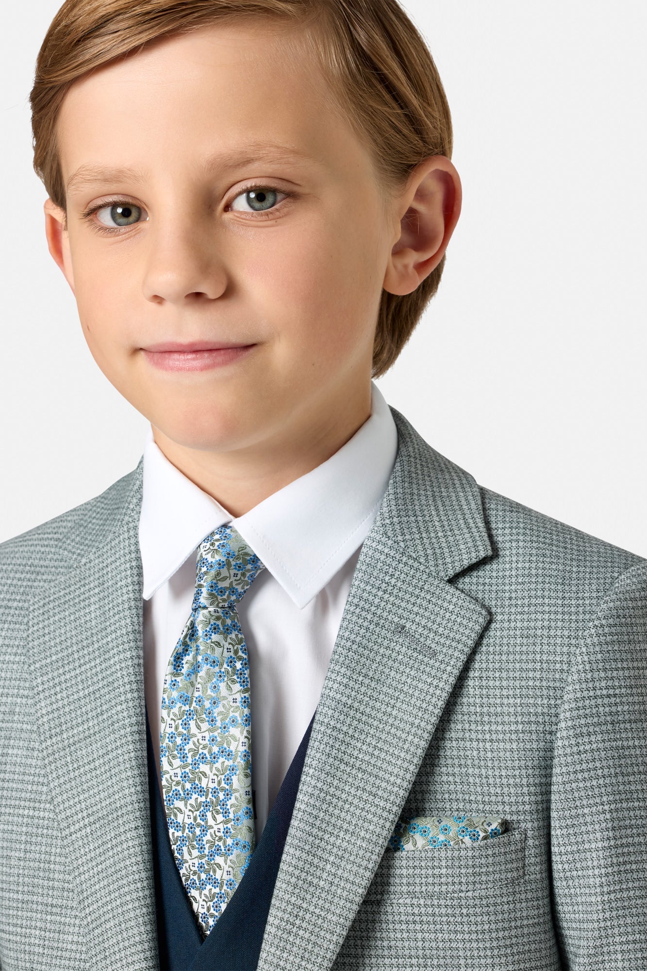 Young boy wearing a sage green checkered blazer with a floral tie on a light background