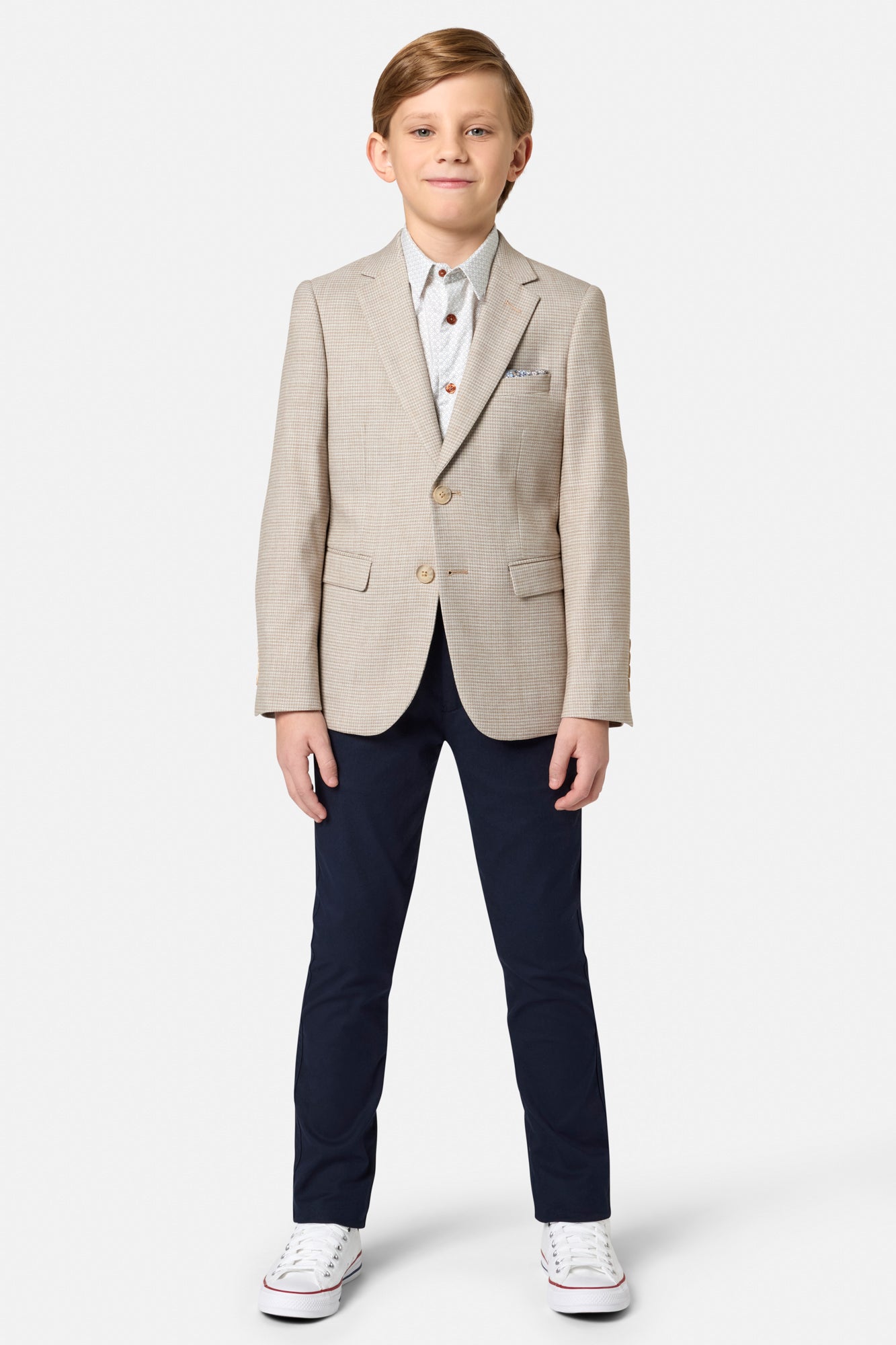 Young boy wearing a beige blazer and navy pants on a white background